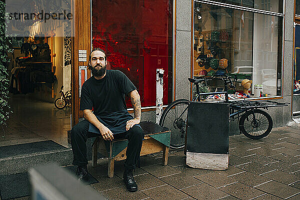 Männlicher Mechaniker sitzt auf einem Tisch vor einem Einzelhandelsgeschäft