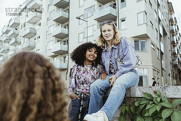 Porträt von lächelnden Freunden durch Stützmauer in der Stadt