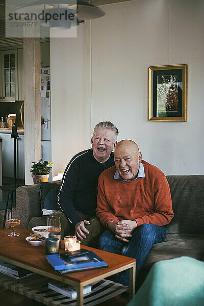 Älteres homosexuelles Paar lachend beim Fernsehen zu Hause im Wohnzimmer