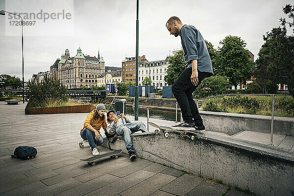 Freunde fotografieren durch Smartphone während männlicher Skater mit Skateboard auf Stützmauer
