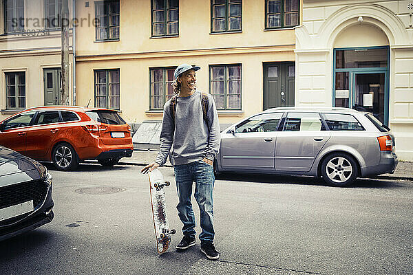 Männlicher Skateboarder mit Hand in der Tasche schaut weg  während er auf der Straße steht