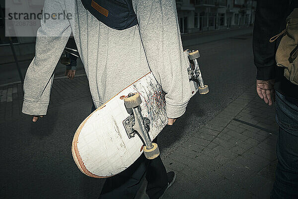 Männliche Freunde mit Skateboard auf dem Fußweg in der Abenddämmerung