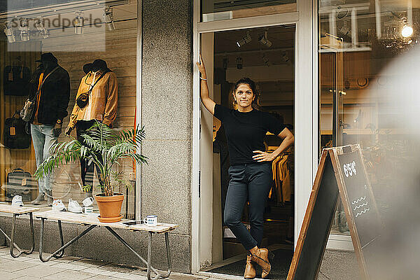 Weibliche Unternehmerin mit Hand auf der Hüfte stehend in der Tür eines Einzelhandelsgeschäfts