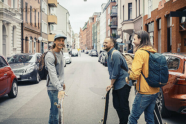 Glückliche Freunde reden  während sie mit Skateboards auf der Straße in der Stadt stehen