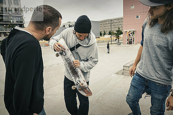 Männliche Freunde schauen auf Skateboard  während sie im Park stehen