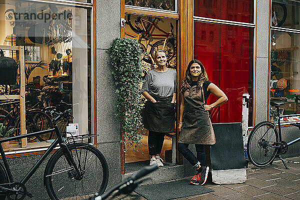 Lächelnde weibliche Mitarbeiter stehen vor der Tür eines Fahrradladens