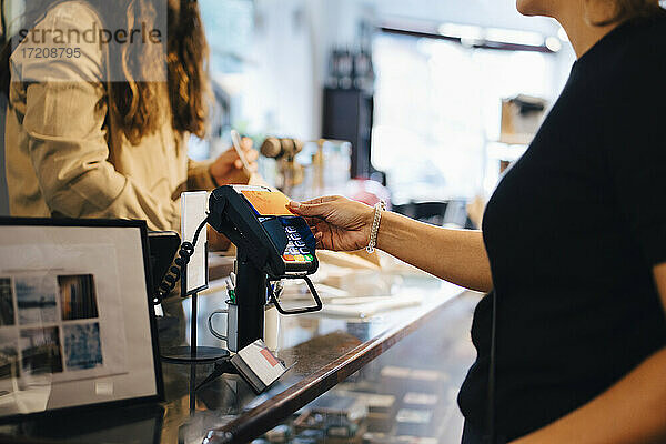 Ausgeschnittenes Bild eines männlichen Kunden  der mit seiner Kreditkarte an die Besitzerin eines Einzelhandelsgeschäfts zahlt