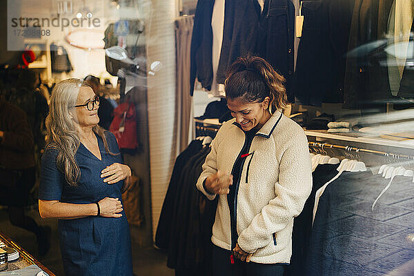 Weibliche Kundin mit warmer Jacke steht neben Geschäftsfrau in Einzelhandelsgeschäft
