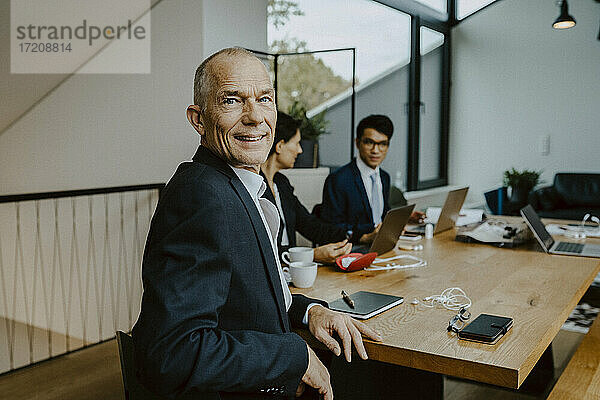 Porträt von Geschäftsmann  während männliche und weibliche Kollegen im Hintergrund im Büro arbeiten