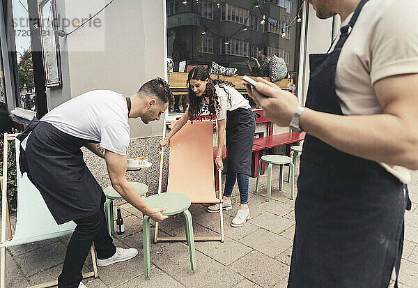 Männliche und weibliche Unternehmer arrangieren Tische und Stühle vor dem Cafe