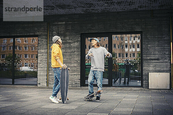 Männliche Freunde unterhalten sich  während sie mit Skateboard auf dem Fußweg stehen