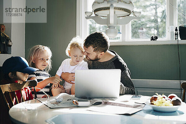 Vater mit Kindern verwendet Laptop über Tisch zu Hause