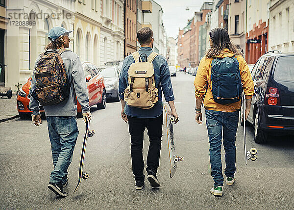Rückansicht von männlichen Freunden mit Skateboards zu Fuß in der Stadt