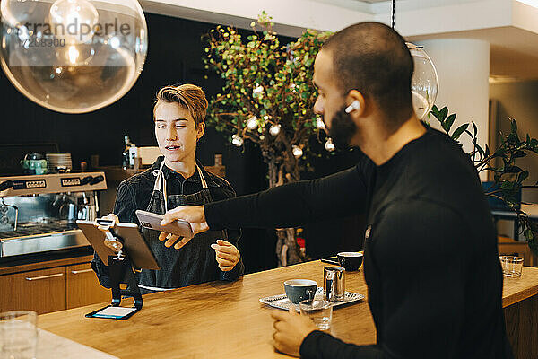 Männlicher Kunde beim kontaktlosen Bezahlen mit dem Smartphone in einem Coffee Shop
