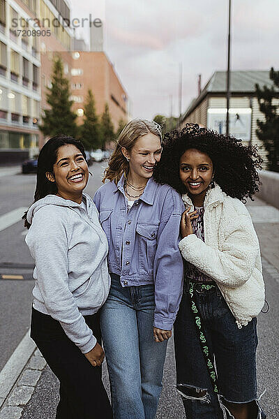 Weibliche Freunde lachen  während sie auf der Straße stehen