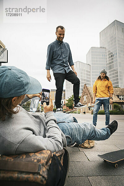 Mann fotografiert  während männlicher Freund auf Fußweg skatet