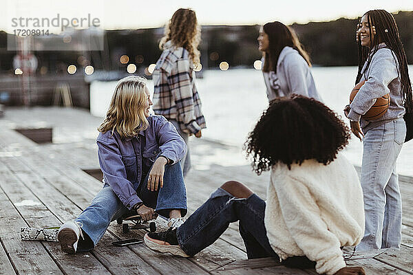 Glückliche weibliche Freunde verbringen Freizeit auf Pier während Sonnenuntergang