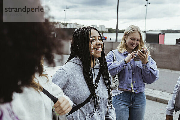 Teenager-Mädchen mit Smartphone stehend mit Freundinnen auf dem Fußweg