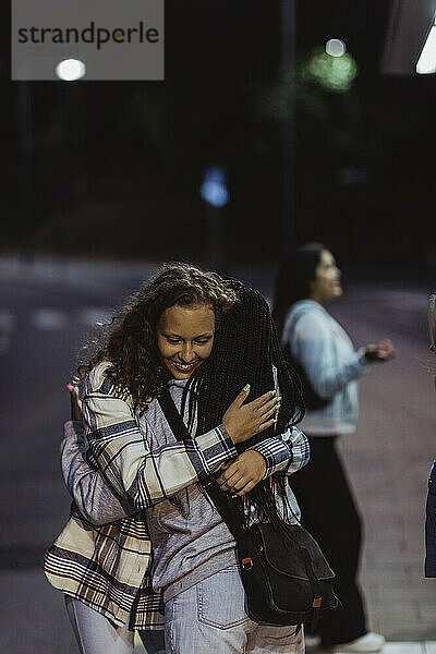 Weibliche Freunde umarmen sich gegenseitig auf der Straße in der Nacht