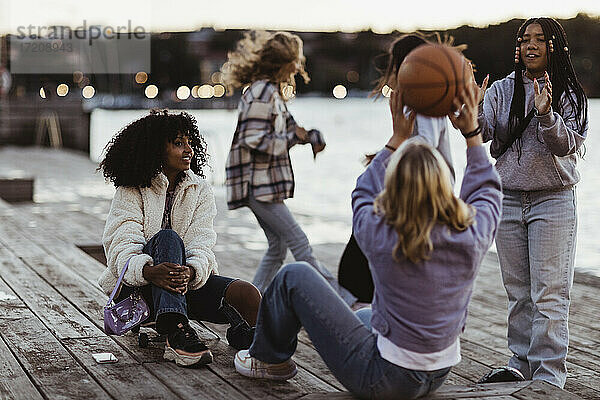 Weibliche Freunde spielen mit Basketball auf Pier bei Sonnenuntergang