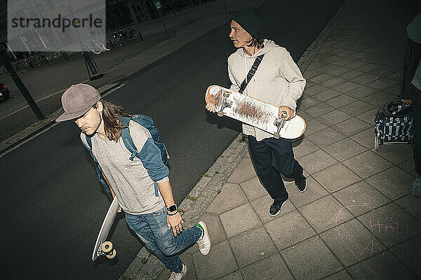 Männliche Freunde mit Skateboard gehen auf dem Bürgersteig