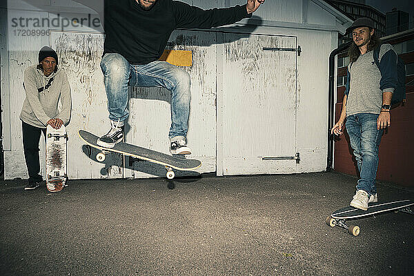 Männlicher Skater mit Skateboard springt von Freunden auf der Straße