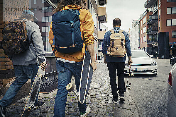 Rückansicht der männlichen Freunde mit Skateboard zu Fuß auf dem Bürgersteig in der Stadt