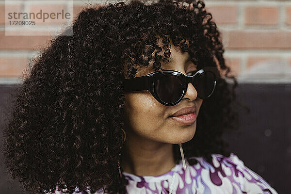 Afrikanisches Teenager-Mädchen mit Sonnenbrille schaut im Freien weg