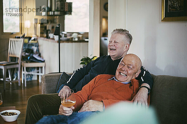 Fröhlich Homosexuelles Paar lachend  während auf dem Sofa im Wohnzimmer sitzen