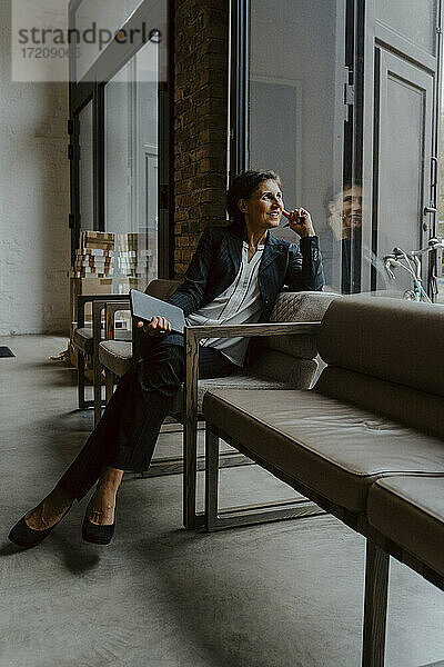 Lächelnde Geschäftsfrau schaut durch  während sie im Büro sitzt
