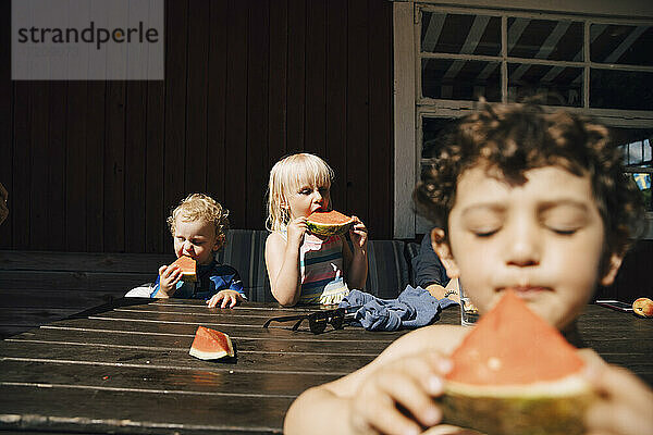 Geschwister essen Obst beim Stehen am Tisch während des sonnigen Tages