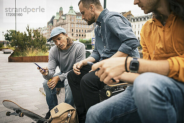 Männliche Skater  die das Smartphone benutzen  während sie auf dem Gehweg sitzen