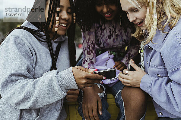 Weibliche Teenager-Freunde  die im Freien ein Mobiltelefon benutzen