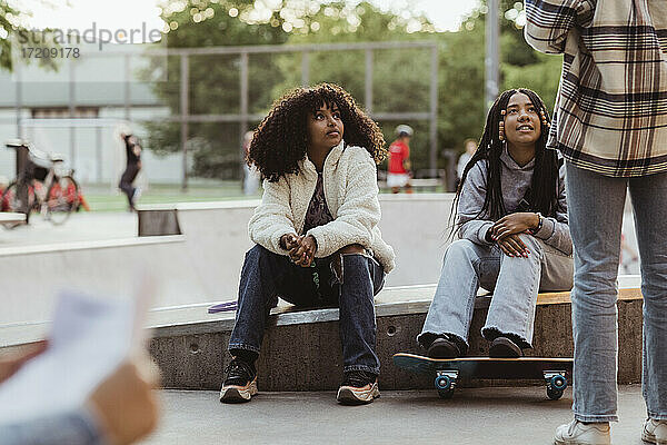 Teenager-Mädchen sitzen auf Stützmauer Blick auf weiblichen Freund in Skateboard-Park