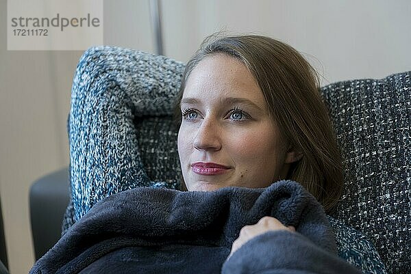 Eine junge Frau liegt in eine Decke eingekuschelt auf einem Sofa in Dorfen  Bayern  Deutschland  Europa