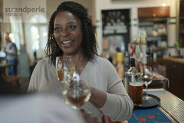 Lächelnde Frau trinkt Weißwein mit Freund an der Bar