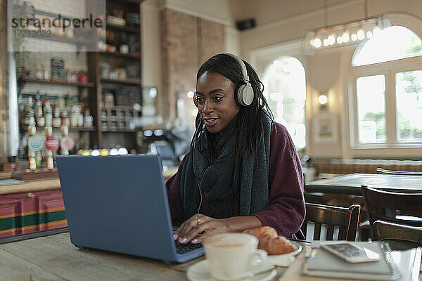 Frau mit Kopfhörer arbeiten am Laptop auf Café Tisch