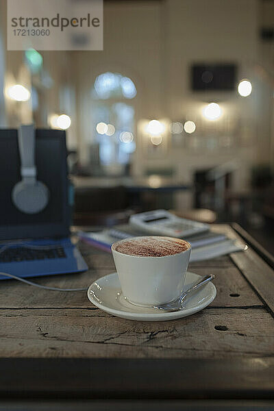 Cappuccino auf Cafe-Tisch neben Laptop