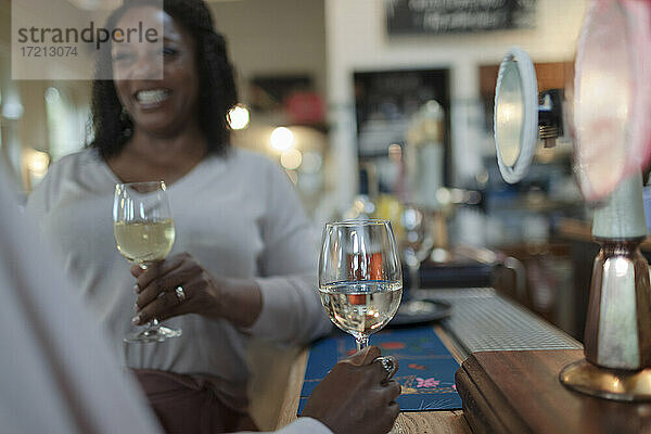 Glückliche Frau trinkt Weißwein mit Freund in Bar