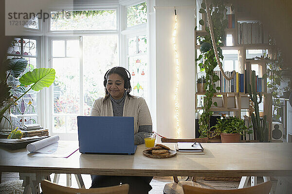 Frau mit Kopfhörer arbeitet von zu Hause aus am Laptop