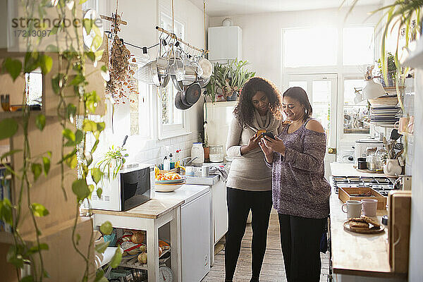 Mutter und Tochter mit Smartphone in der Küche