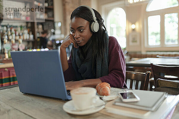 Junge Geschäftsfrau mit Kopfhörer arbeiten am Laptop im Café