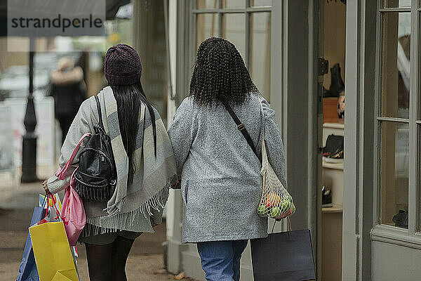Mutter und Tochter mit Einkaufstaschen zu Fuß auf dem Bürgersteig