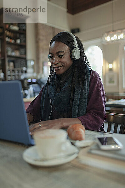 Junge Frau mit Kopfhörer arbeiten am Laptop im Café