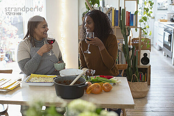 Mutter und Tochter kochen und trinken Rotwein am Tisch
