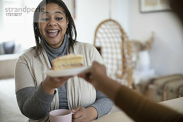 Glückliche aufgeregte Frau greift nach einem Stück Kuchen