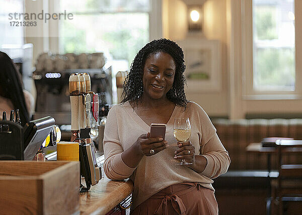 Frau mit Smartphone genießt Weißwein in Bar
