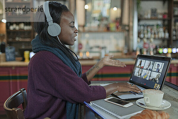 Junge Frau mit Kopfhörer Video-Chat mit Kollegen im Café