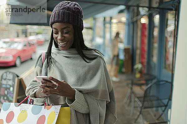 Junge Frau mit Einkaufstasche mit Smartphone auf dem Bürgersteig