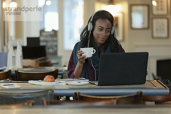 Junge Frau mit Kopfhörer trinken Kaffee am Laptop im Café